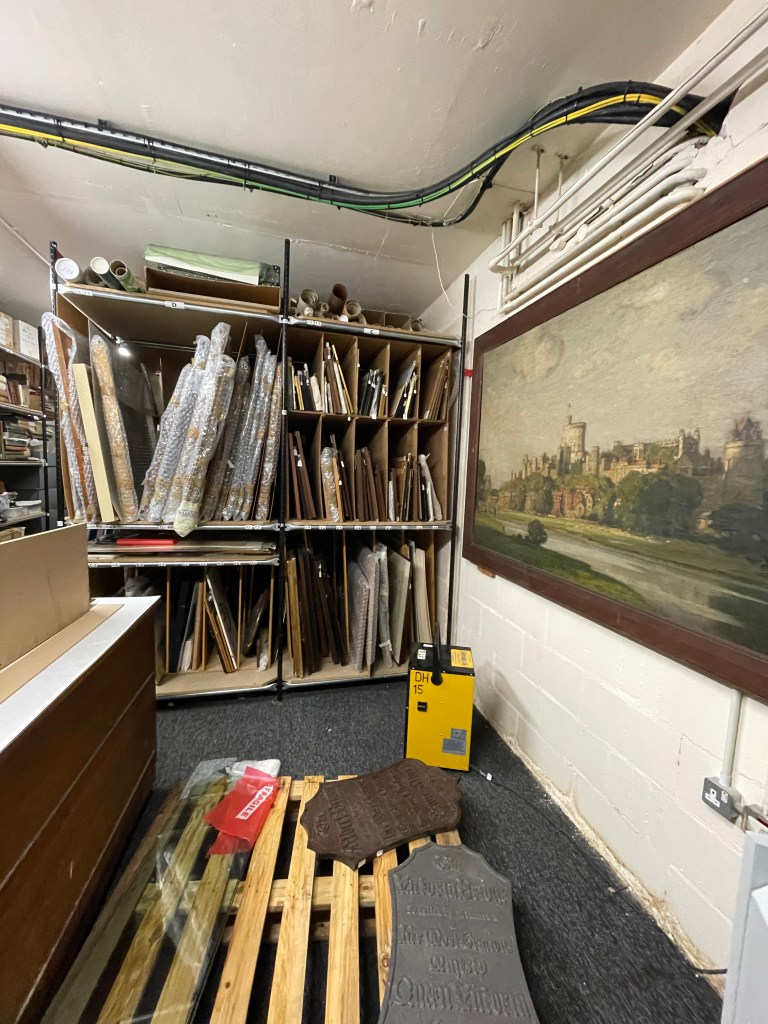 Interior of the Archive Store showcasing stacks of framed artworks and manuscripts, with a large painting of Windsor in the background.