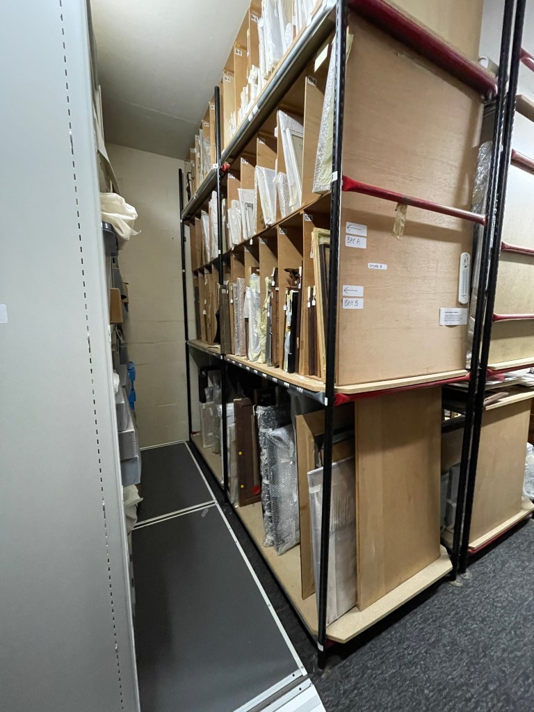 Interior view of the Archive Store, showcasing shelves filled with framed items and archival boxes.