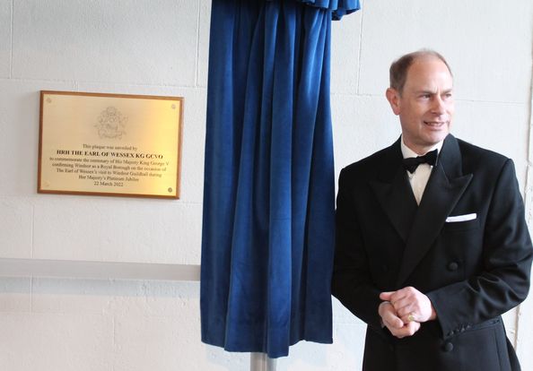 Prince Edward in formal attire stands next to a plaque commemorating the 2022 re-opening, with blue fabric draped above the plaque.