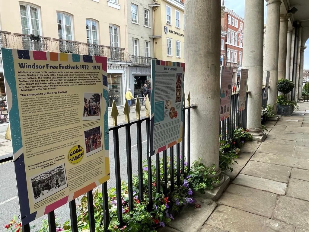 Exhibition panels showcasing the Windsor Free Festivals from 1972 to 1974, displayed outdoors on the historic Corn Exchange, surrounded by plants and flowers.