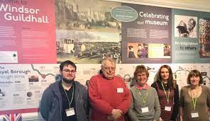 A group of Friends of all ages standing in front of an informational display about the Windsor Guildhall and the local museum.