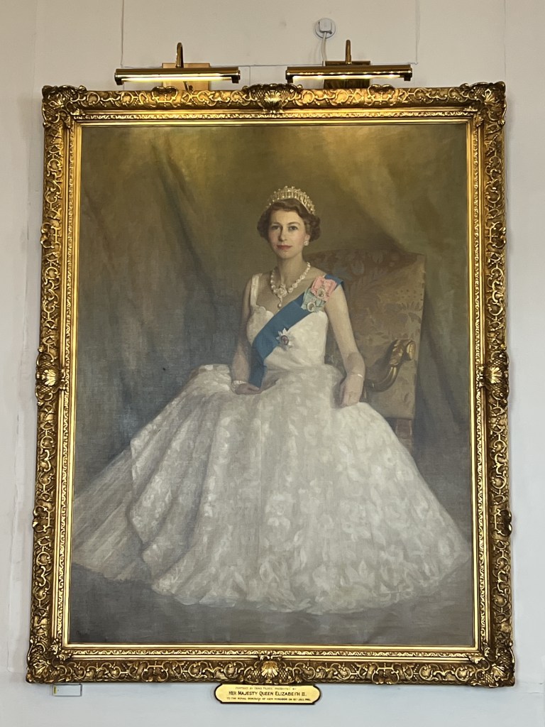 Portrait of Queen Elizabeth II in a white gown, adorned with a necklace and tiara, framed in an ornate golden frame.
