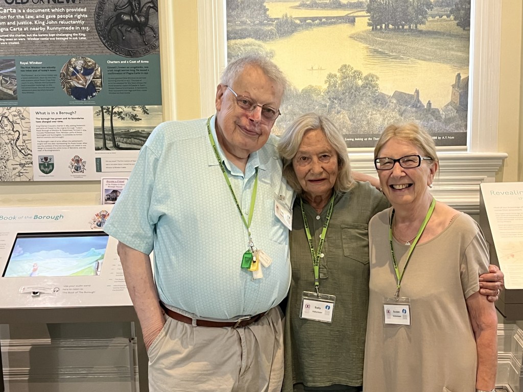 Three smiling Friends of the Museum standing together iside our museum, with informative displays in the background.