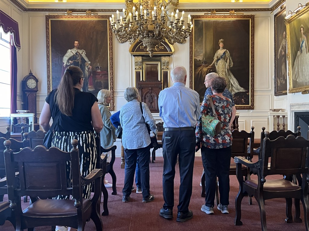 Group of visitors observing historical portraits in Guildhall with a chandelier.