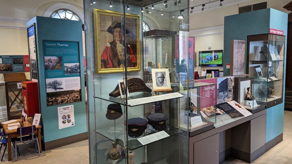 Interior view of the Windsor & Royal Borough Museum, showcasing exhibits including a portrait and various artifacts displayed in glass cases.