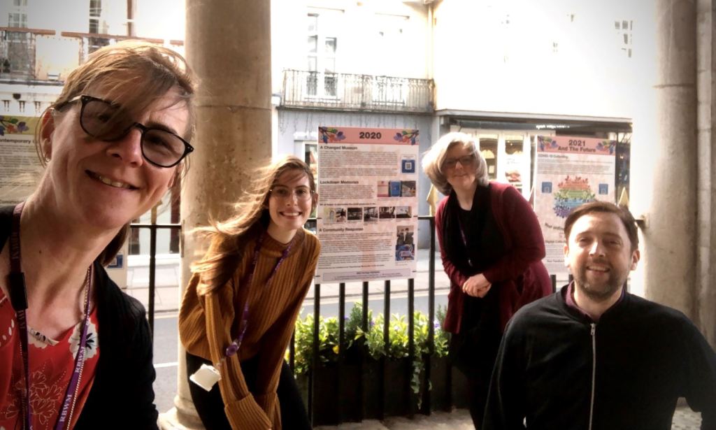 Four museum staff members posing together outside, with exhibition panels in the background.