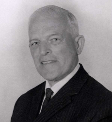 A black and white portrait of a Maitland Underwood smiling, wearing a suit and tie.