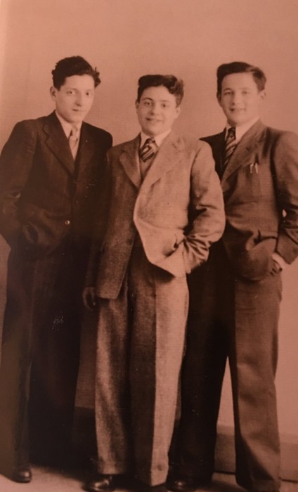 Three young boys in formal suits, smiling and standing together for a photograph.
