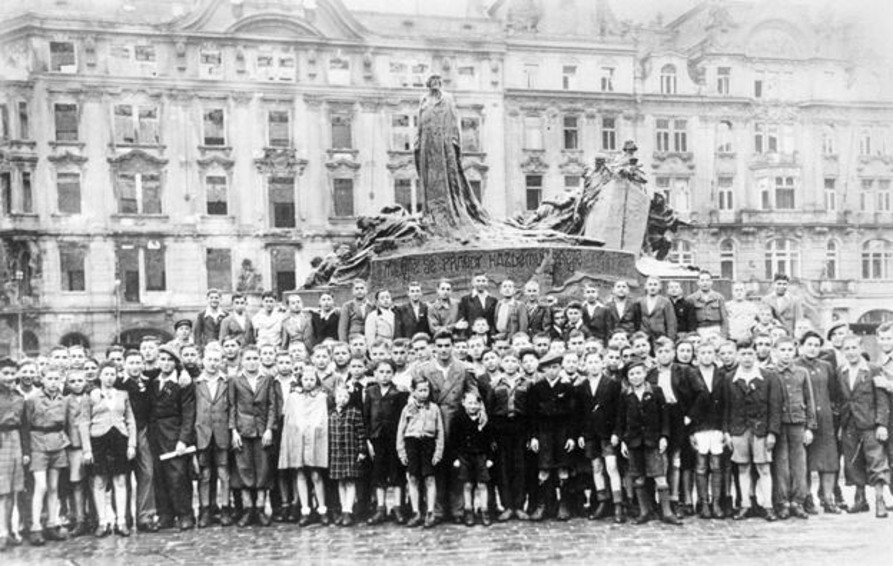 Group of children and young people, survivors of the Holocaust, gathered in front of a monument in Prague.