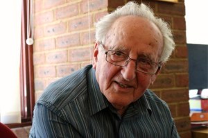 Close-up portrait of an elderly Ivor Perl with glasses and grey hair, smiling softly in a casual setting.