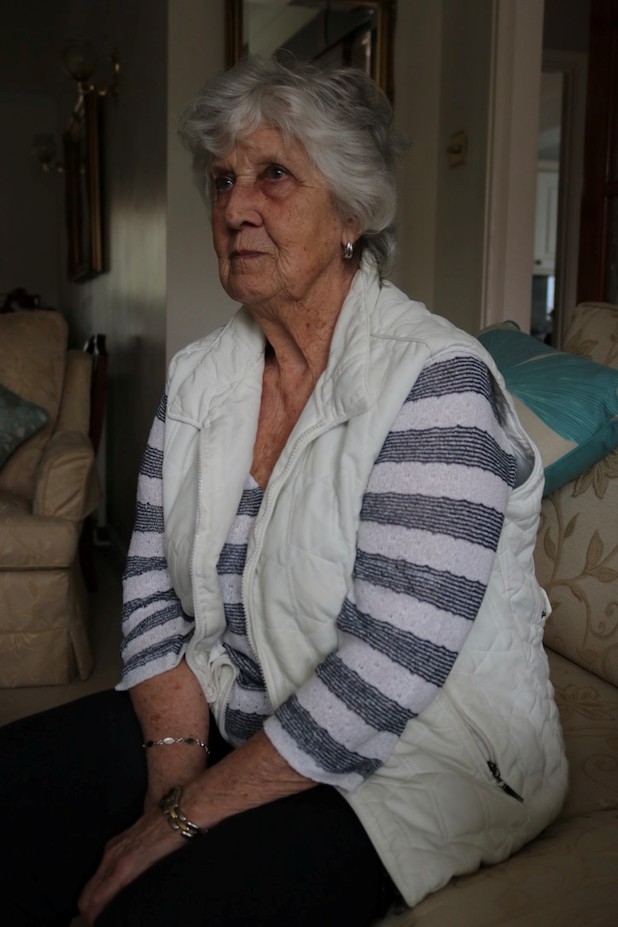 An elderly Margaret Nutley with gray hair, seated and looking contemplative, dressed in a striped shirt and a white vest.