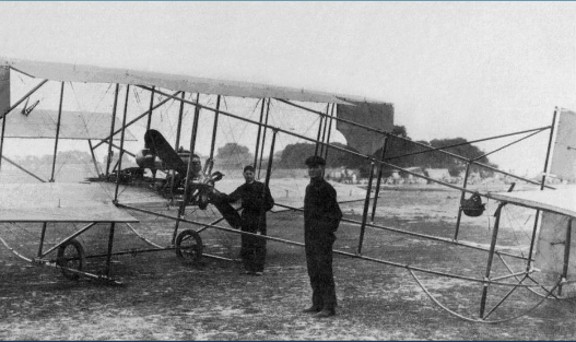 Historical photo of two men beside an early biplane aircraft on a runway, showcasing early aviation technology.