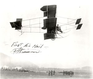 Historic photograph of the first airmail flight, featuring an early powered aircraft in flight with onlookers watching from below.