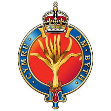 Emblem of the Band of the Welsh Guards featuring a golden leek with a crown above, set against a red background.