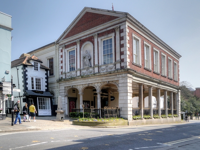 The historic Guildhall in Windsor featuring classical architecture, with columns and a statue, surrounded by trees and shops.