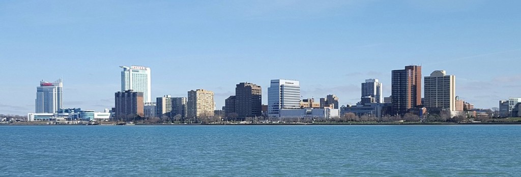 Panoramic view of Windsor, Ontario skyline across the Detroit River, showcasing modern buildings and clear blue skies.