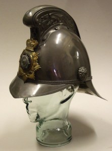 John Tull's vintage volunteer fireman's helmet displayed on a glass head, featuring intricate details and a badge.