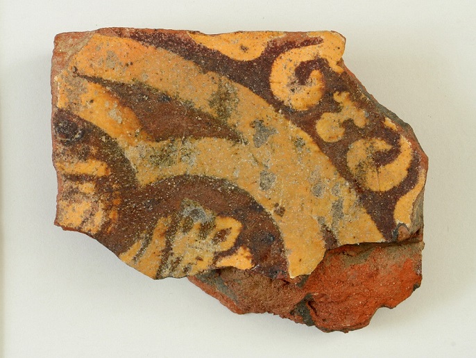 A piece of pottery with intricate patterns in orange, brown, and yellow colors, showcasing historical decorative design.